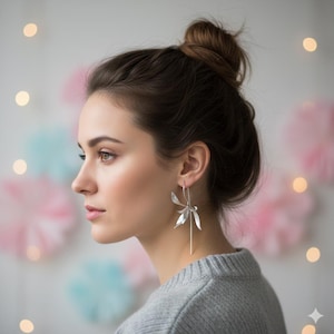 K&ouml;nnte beinhalten: Eine Frau tr&auml;gt silberne Ohrh&auml;nger mit floralem Design. Die Ohrringe sind lang und h&auml;ngen vom Ohr. Die Frau tr&auml;gt einen grauen Pullover und hat ihr Haar zu einem Dutt hochgesteckt.