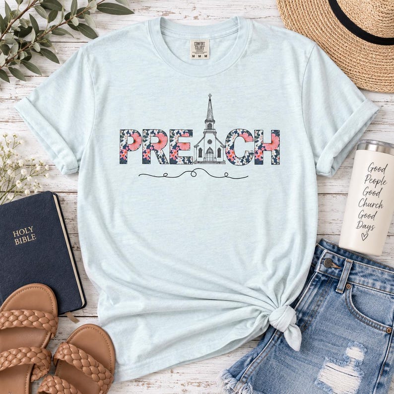 以下が含まれることがあります： 花柄で描かれた「PREACH」の文字がプリントされたライトブルーの半袖Tシャツ。文字の「A」の部分は教会のイラストになっています。クルーネックで、右下の裾が結ばれたデザインの衣類です。