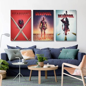 May include: Three framed Deadpool film posters. The first shows Deadpool's mask and crossed swords against a red backdrop with the text "HEADPOOL". The second shows Deadpool standing with a fiery background. The third shows Deadpool upside down.