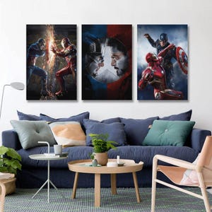 May include: Three framed canvas prints depicting Marvel characters. One shows Captain America and Iron Man clashing, another features their faces, and the third shows them in action. The prints are displayed above a blue sofa.