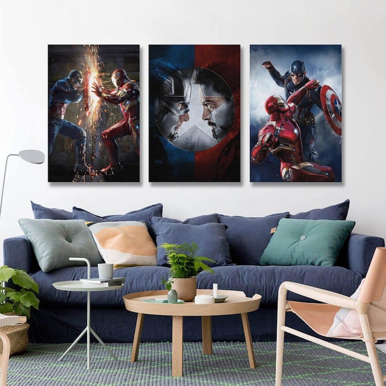 May include: Three framed canvas prints depicting Marvel characters. One shows Captain America and Iron Man clashing, another features their faces, and the third shows them in action. The prints are displayed above a blue sofa.