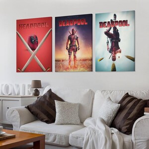May include: Three framed canvas prints showcasing Deadpool artwork. The prints depict Deadpool in action poses, with the title "Deadpool" in red. The first print features Deadpool's mask and crossed swords on a red background.