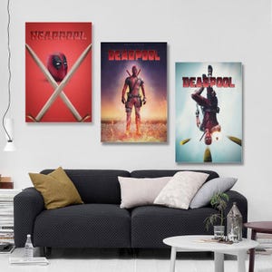 May include: Three Deadpool film posters displayed on a wall above a black sofa. The posters feature the Deadpool character in various action poses, with the title "Deadpool" in bold red letters. The first poster has the text "Headpool".