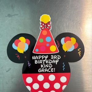 May include: A die-cut sign shaped like a mouse head with black ears, a red polka-dot base, and a party hat on top. The sign features colorful balloons, confetti, and the text "HAPPY 3RD BIRTHDAY KIND GRACE!" printed in white on the black center section.
