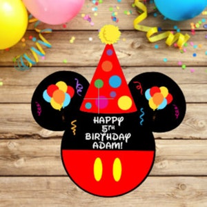 May include: A black and red mouse-shaped birthday sign featuring a red party hat with colorful polka dots, two black ears with balloon illustrations, and the white text "HAPPY 5TH BIRTHDAY ADAM!" above two yellow oval shapes on a red base.