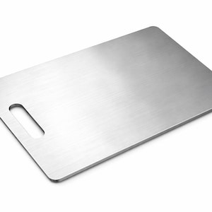 May include: A rectangular, brushed stainless steel cutting board with a handle cutout. The board has rounded corners and a smooth, metallic surface. The handle is a rectangular cutout on the left side.
