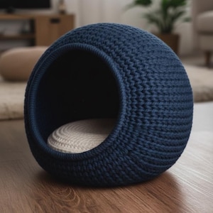 May include: A navy blue, spherical pet bed with a woven texture. The bed has a circular opening and a cream-colored cushion inside. The pet bed is made of a thick, durable material and sits on a wooden floor.