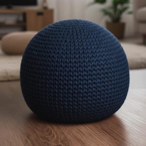 May include: A navy blue, spherical knitted pouf. The pouf is made of a thick, textured yarn and sits on a wooden floor. The knitted design is visible, creating a cozy and inviting aesthetic. This decorative item is suitable for living rooms and bedrooms.