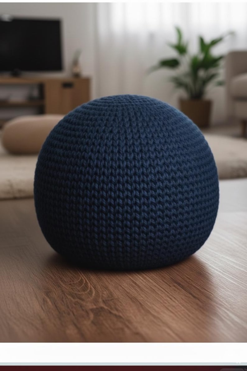 May include: A navy blue, spherical knitted pouf. The pouf is made of a thick, textured yarn and sits on a wooden floor. The knitted design is visible, creating a cozy and inviting aesthetic. This decorative item is suitable for living rooms and bedrooms.
