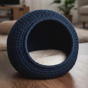 May include: A navy blue, round pet bed with a woven texture. The bed has a circular opening and a cream-colored, woven interior cushion. The bed is placed on a wooden floor, suggesting a cozy indoor setting for pets.