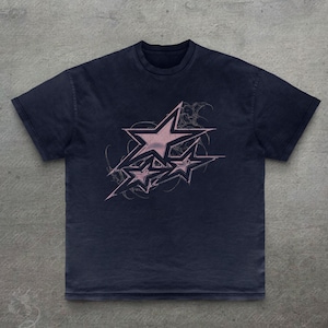 Op de afbeelding: Marineblau T-shirt met een roze sterrenontwerp. De afbeelding toont meerdere sterren met een distressed, grunge stijl. De tee heeft een ronde hals en korte mouwen, ideaal voor dagelijks gebruik. Het shirt is gemaakt van zacht materiaal.