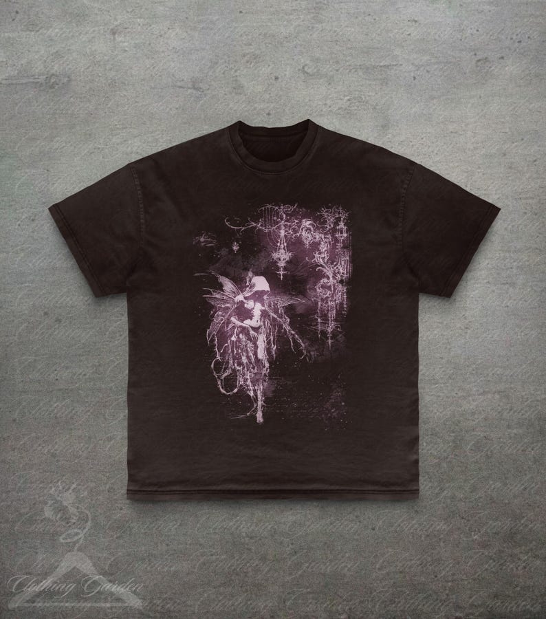 May include: Dark brown t-shirt with a purple fairy illustration. The design features a winged figure with a flowing gown and gothic details. The tee has a crew neck and short sleeves. The image has a vintage look.