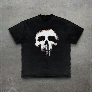 Op de afbeelding: Een zwart T-shirt met korte mouwen en een grote, gecentreerde afbeelding van een witte schedel. Het schedelontwerp heeft een verweerde, getextureerde uitstraling met verticale druppels aan de onderkant voor een versleten visueel effect.