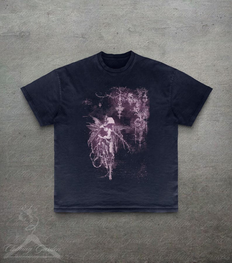 May include: Dark navy blue t-shirt with a faded purple illustration of a fairy with wings and decorative background details. The shirt has a crew neck and short sleeves. The text "Clothing Garden" is in the bottom left corner.