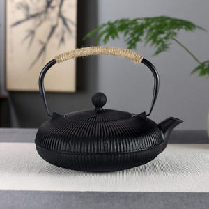 May include: A white ceramic mug with a black handle and the text "But First, Coffee" in a bold, black font. The mug is set against a neutral background, highlighting its simple design.