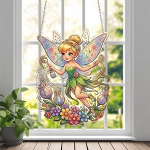 May include: A decorative fairy window hanging. The fairy has blonde hair, green dress, and colorful wings. She is surrounded by flowers and a glittery border. The hanging is suspended by a silver chain.