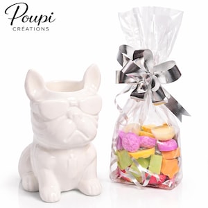 Peut inclure: Un pot en céramique blanc en forme de bouledogue avec des lunettes de soleil, à côté d'un sac en cellophane noué avec un nœud argenté. Le sac contient des fondants parfumés colorés. La marque "Poupi Créations" est visible.