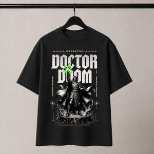 Może przedstawiać: Czarny t-shirt z krótkim rękawem z nadrukiem graficznym przedstawiającym Doctora Dooma. Wzór zawiera tekst "CELESTIAL DOCTOR DOOM", "LATVERIAN SOVEREIGN" oraz "MASTER OF DARK ARTS" z efektem zielonej świecącej energii w jednej dłoni.