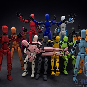 May include: A collection of multi-coloured articulated action figures, including red, blue, yellow, and green, are displayed against a dark backdrop. The figures have a humanoid design with visible joints and black hands. The logo "SHUMAKER STUDIOS" is visible.