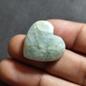 May include: A heart-shaped polished gemstone with a pale mint green and white marbled appearance. The stone features a smooth, glossy surface with visible internal fractures and natural veining patterns throughout its translucent structure.