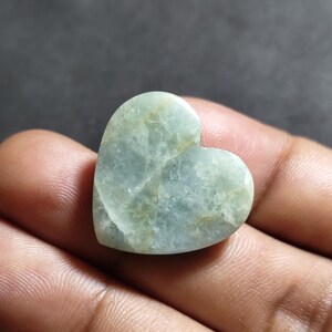 May include: A heart-shaped polished stone with a pale mint green color and translucent quality. The surface features visible internal fractures and subtle golden-brown veining throughout the smooth, rounded edges of the gemstone.