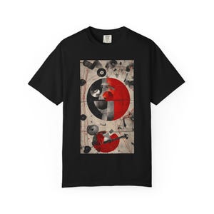 May include: Black t-shirt with a rectangular graphic of abstract shapes. The design features a large red circle, a black and white yin-yang-like shape, and other geometric elements. The shirt is made of a soft material.