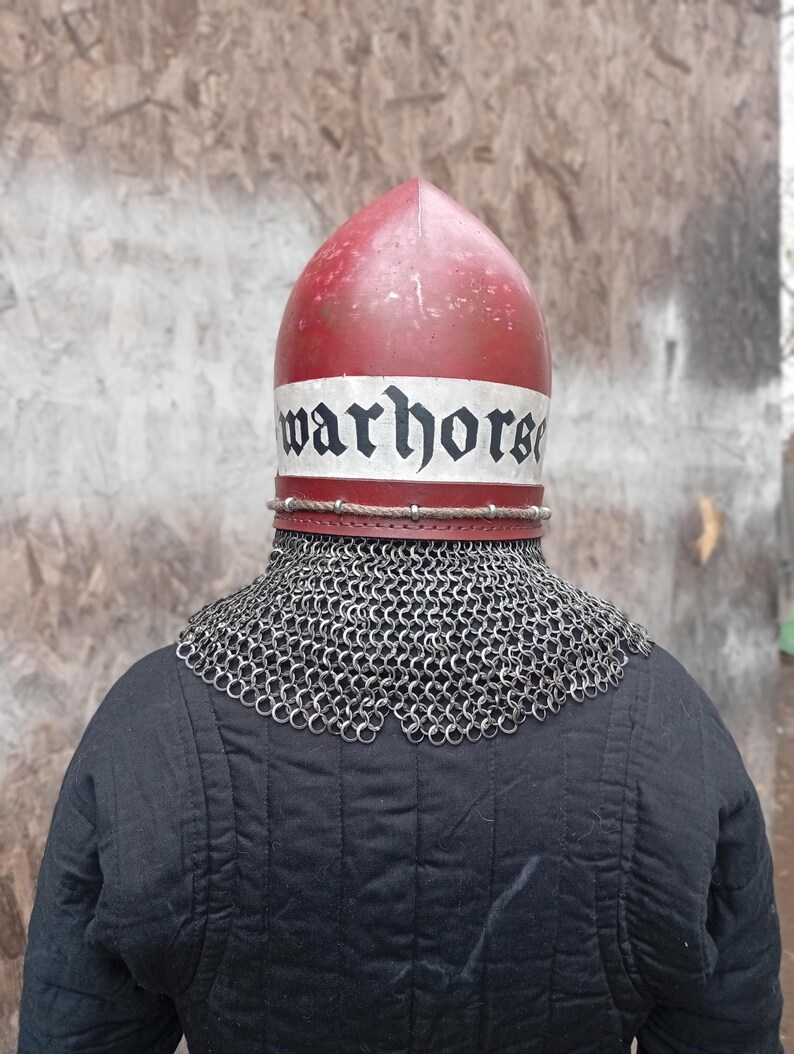 May include: A red and white medieval helmet with the word "warhorse" printed on the front. The helmet is worn over a chainmail collar and a black quilted garment.