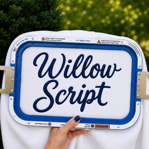 May include: A white fabric piece secured in a blue 5.5 inch Mighty Hoop embroidery frame. The fabric features the dark blue embroidered text Willow Script. The frame includes warning labels about magnets and electronic devices in English.