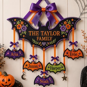 Op de afbeelding: Een zwarte, vleermuisvormige wandhanger met de tekst THE TAYLOR FAMILY, voorzien van vijf kleinere hangende vleermuisornamenten gepersonaliseerd met de namen Aria, Jaxon, Harper, Evie en Noah, geaccentueerd met paarse en oranje linten.