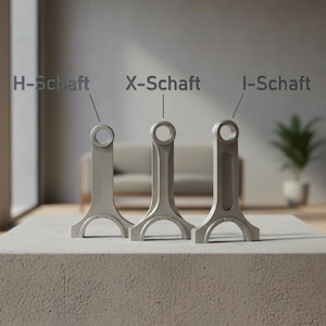 Könnte beinhalten: Drei silberfarbene Pleuel, beschriftet mit H-Schaft, X-Schaft und I-Schaft, werden auf einem Betonblock präsentiert. Die Pleuel haben eine charakteristische Form mit einer kreisförmigen Öffnung oben und einer gebogenen Basis. Der Hintergrund zeigt ein modernes Interieur mit Sofa und Pflanze.