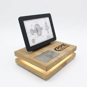 Könnte beinhalten: Ein E-Reader mit einer mechanischen Zeichnung liegt auf einem Holzständer mit einem leuchtenden Licht. Der Ständer hat eine Metallplatte mit Text und dem Logo "PPE Power Plant Engineering".