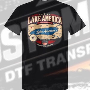 以下が含まれることがあります： Lake Americaと書かれた地図のグラフィックプリントが施された黒の半袖Tシャツ。デザインにはコンパス、Lake America、The Greatest Lake In The Nation、New York、Canada、Big. Beautiful. American.という文字と盾の紋章が含まれています。