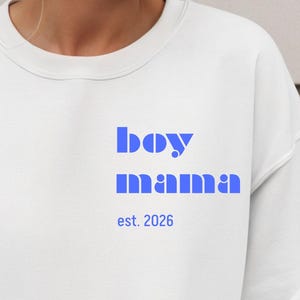 Może przedstawiać: Biała bluza z niebieskim napisem "boy mama" i datą "est. 2026". Bluza ma okrągły dekolt.