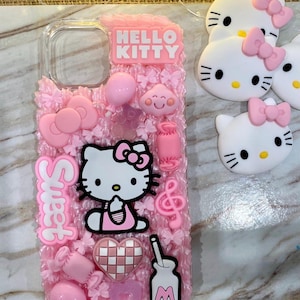 Può includere: Una custodia trasparente per telefono decorata con abbellimenti rosa a tema Hello Kitty. La custodia presenta le parole "Hello Kitty" e "Sweet" in un carattere a bolle. Ulteriori decorazioni includono un personaggio di Hello Kitty, fiocchi, cuori e altri ciondoli rosa.