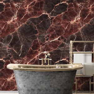 Puede incluir: Un baño lujoso con una pared con diseño de mármol en tonos burdeos, negro y blanco. Una bañera gris con detalles dorados es el punto focal, complementada con un toallero dorado y una planta en maceta.