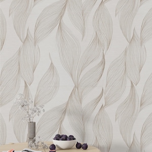 May include: Cream-colored wallpaper with a repeating pattern of stylized, flowing leaves in shades of brown. A round wooden table holds a vase with white flowers, a bowl of figs, and an open book.