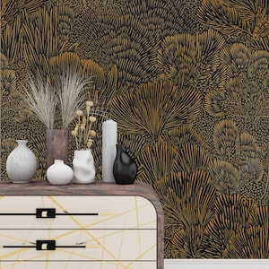 May include: A decorative chest of drawers with a cream-colored front and gold geometric lines. The drawers are topped with a collection of vases, candles, and dried plants. The background is a black and gold botanical wallpaper.