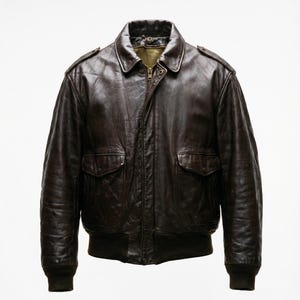 Può includere: Giacca bomber in pelle marrone scuro con chiusura a zip, due tasche frontali e polsini e orlo a coste. La giacca ha un colletto classico e spalline. La pelle presenta un aspetto invecchiato.