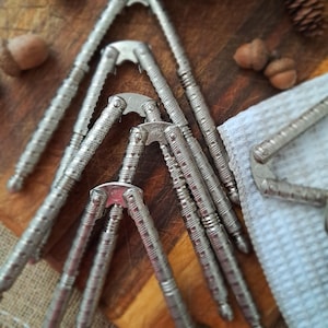 May include: Several silver nutcrackers displayed on a wooden board. The metal nutcrackers have a textured pattern. Acorns and a small pine cone are also visible, alongside a white cloth.