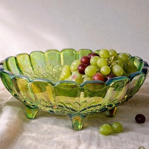 Peut inclure: Un saladier en verre vert irisé avec un bord festonné et trois petits pieds. Le saladier est rempli de raisins verts et rouges. Le saladier présente un motif de feuilles à l'intérieur.