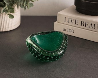 May include: A deep emerald green glass bowl featuring a thick, rounded rim and a distinct bullicante technique with numerous small air bubbles trapped within the glass walls. The bowl has an organic, asymmetrical shape with a smooth, polished finish.