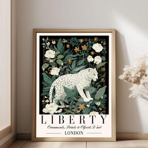 May include: A framed art print featuring a white leopard amidst lush greenery and white roses against a black background. The print includes the text "LIBERTY" and "LONDON" with additional text below. The artwork is in a gold frame.