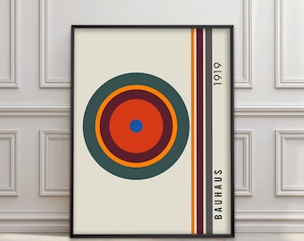 May include: A framed art print featuring a geometric design with a central circular pattern in shades of orange, green, and blue. Vertical stripes in orange, brown, and gray are on the right side. The word "BAUHAUS" and the number "1919" are printed vertically.