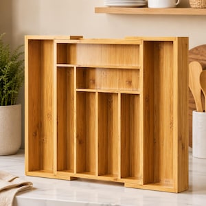 May include: A light brown bamboo cutlery organizer featuring multiple vertical and horizontal compartments of varying sizes. The expandable tray has a natural wood grain finish and is designed with a rectangular frame to hold kitchen utensils.