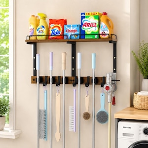 May include: A wall-mounted storage rack with a wooden shelf and black metal frame. The top shelf holds cleaning supplies including Tide, Ariel, and Downy bottles. Below, a rack with hooks holds various cleaning tools, brushes, and a vacuum.