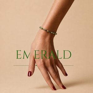 Könnte beinhalten: Ein Perlenarmband aus kleinen, runden, facettierten grünen Steinen. Das Wort EMERALD ist in großen, dunkelgrünen Großbuchstaben in der Mitte des Bildes gedruckt, mit einer dünnen horizontalen Linie unterhalb des Textes.