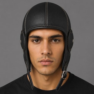 May include: A black leather aviator-style cap featuring prominent tan contrast stitching along the seams. The headwear includes integrated ear flaps with circular side panels and a functional metal buckle strap closure positioned under the chin.