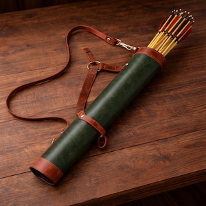 May include: A dark green leather quiver with brown leather accents and a shoulder strap. The quiver is filled with arrows with red and yellow fletching. The quiver is resting on a wooden surface.