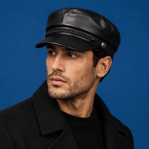 May include: A black leather baker boy cap featuring a structured crown, a short stiff brim, and a decorative braided band across the front. The band is secured on both sides by small, circular silver-toned metal buttons, adding detail to the smooth finish.