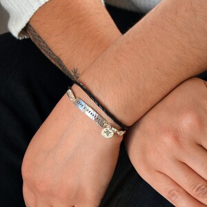 May include: Two bracelets are shown. One is a black braided leather bracelet with a silver charm. The other is a silver bracelet with the words "TYPE 2 DIABETES" stamped on it. The bracelets are worn on a person's wrist.